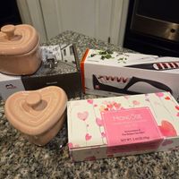 The main content is a collection of gifts on a granite countertop. The gifts include two Staub Lagotte pots, a Mondose chocolates box, a Zwilling 5-in-1 knife and scissor sharpener, and a Mini Cocotte box. The objects are stationary with no motion. The background features a kitchen setting with a black oven.