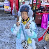 可能是小孩、牛角扣大衣、帽子、羽絨外套、滑雪坡和顯示的文字是「可口可 让我们 乐 乐 杏一起 让我们乐都一起 6 起 ROLTS HTM 0 12 SPACE 0 」的圖像